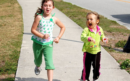 Two young girls running on sidewalk